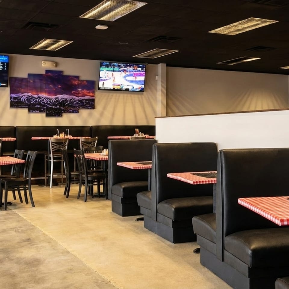 Restaurant interior with black booths, checkered tablecloths, high-top tables, and multiple TVs showing sports.
