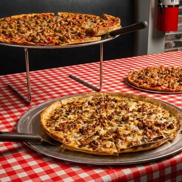 Three pizzas with various toppings on a red and white checkered tablecloth.