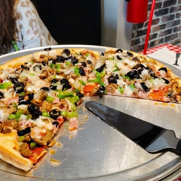 A large pizza with multiple toppings, including olives, peppers, and sausage, on a metal tray.